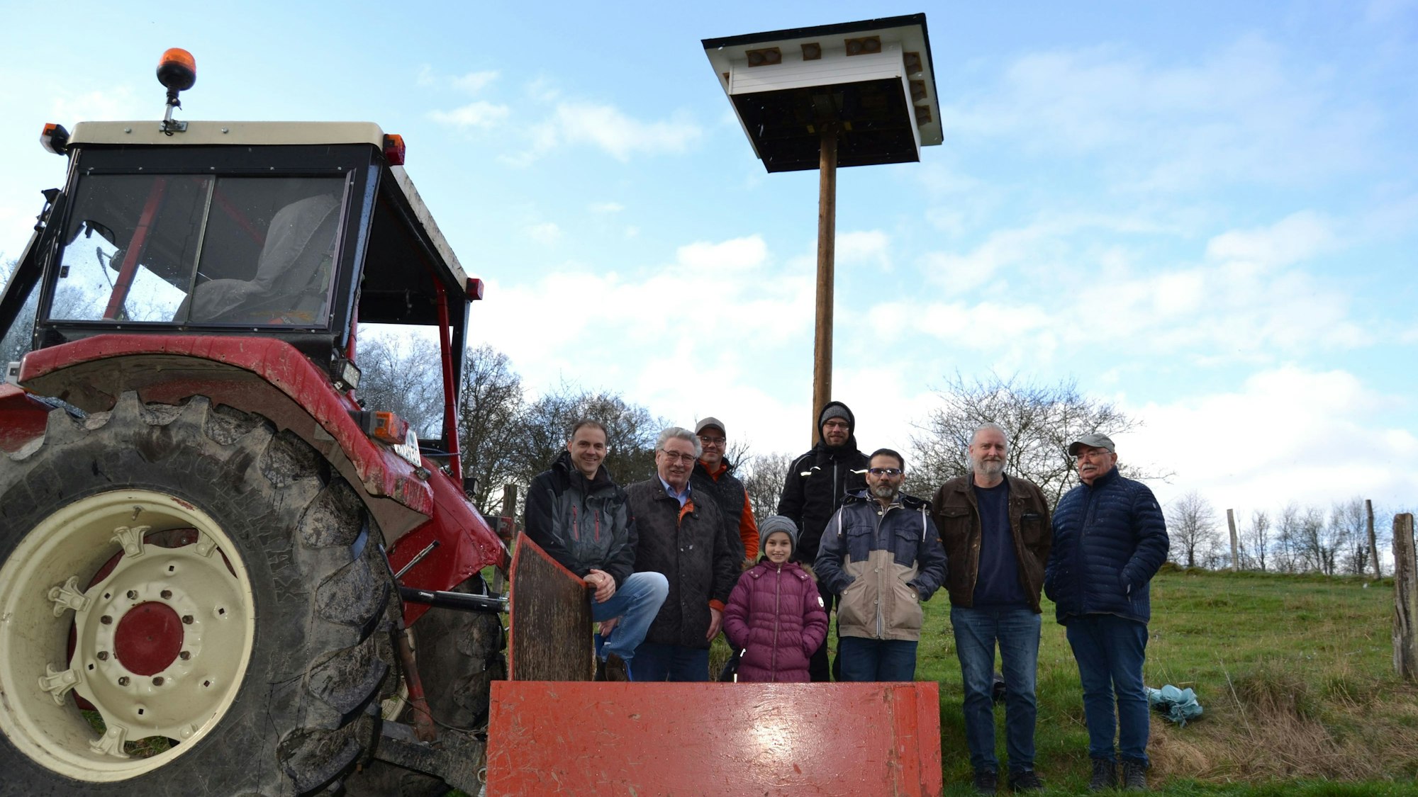 Sieben Männer und ein Mädchen stehen an einem Trecker und vor einem in die Höhe ragenden Nistplatz.