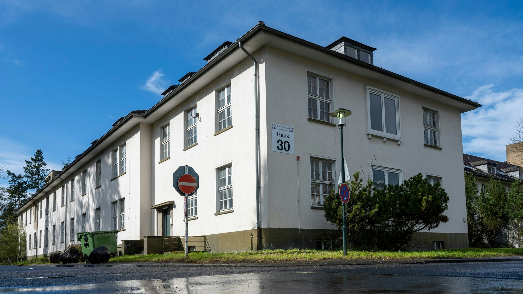 Zu sehen ist ein zweistöckiger, weiß getünchter Gebäudekomplex mit zahlreichen Sprossenfenstern. Darüber schließt sich ein überhängendes Dach mit Dachgauben an. Die Hausnummer 30 ist deutlich zu erkennen. Vor dem Gebäude befindet sich eine kleine Rasenfläche, davor Straße.