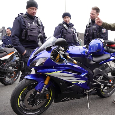 Eine Polizeibeamtin und zwei Polizeibeamte schauen auf ein blaues Motorrad.