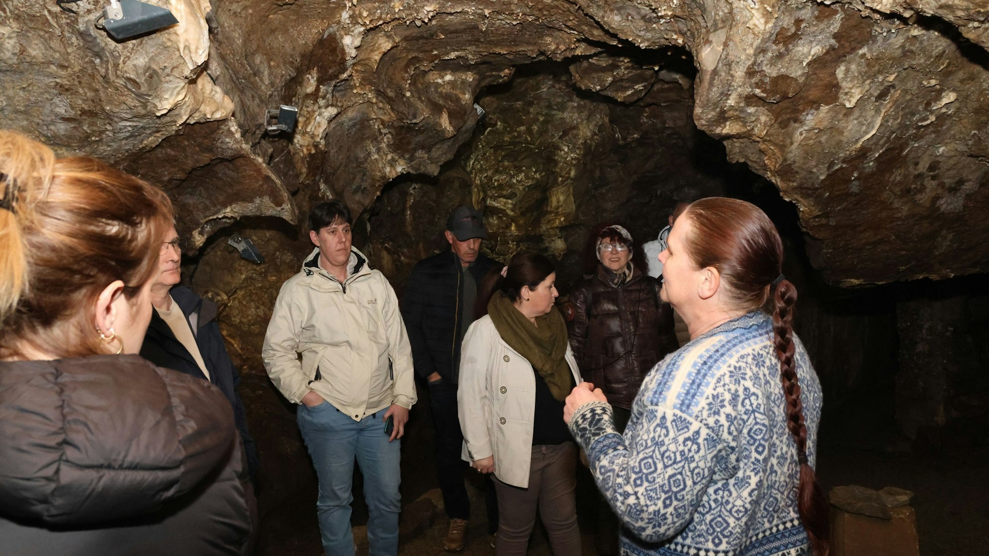Mehrere Männer und Frauen stehen in einer Höhle. Sie nehmen an einer Führung teil und hören der Leiterin zu.