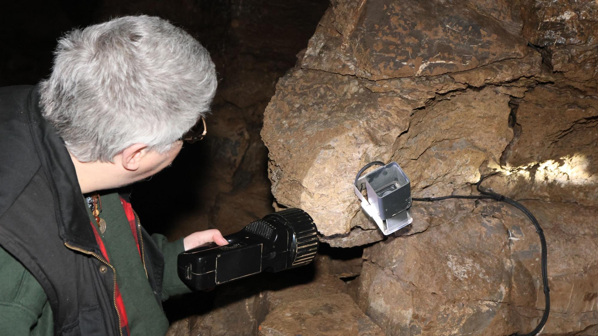 Eine Frau leuchtet in einer Höhle mit einer großen Taschenlampe auf eine defekte Lampe