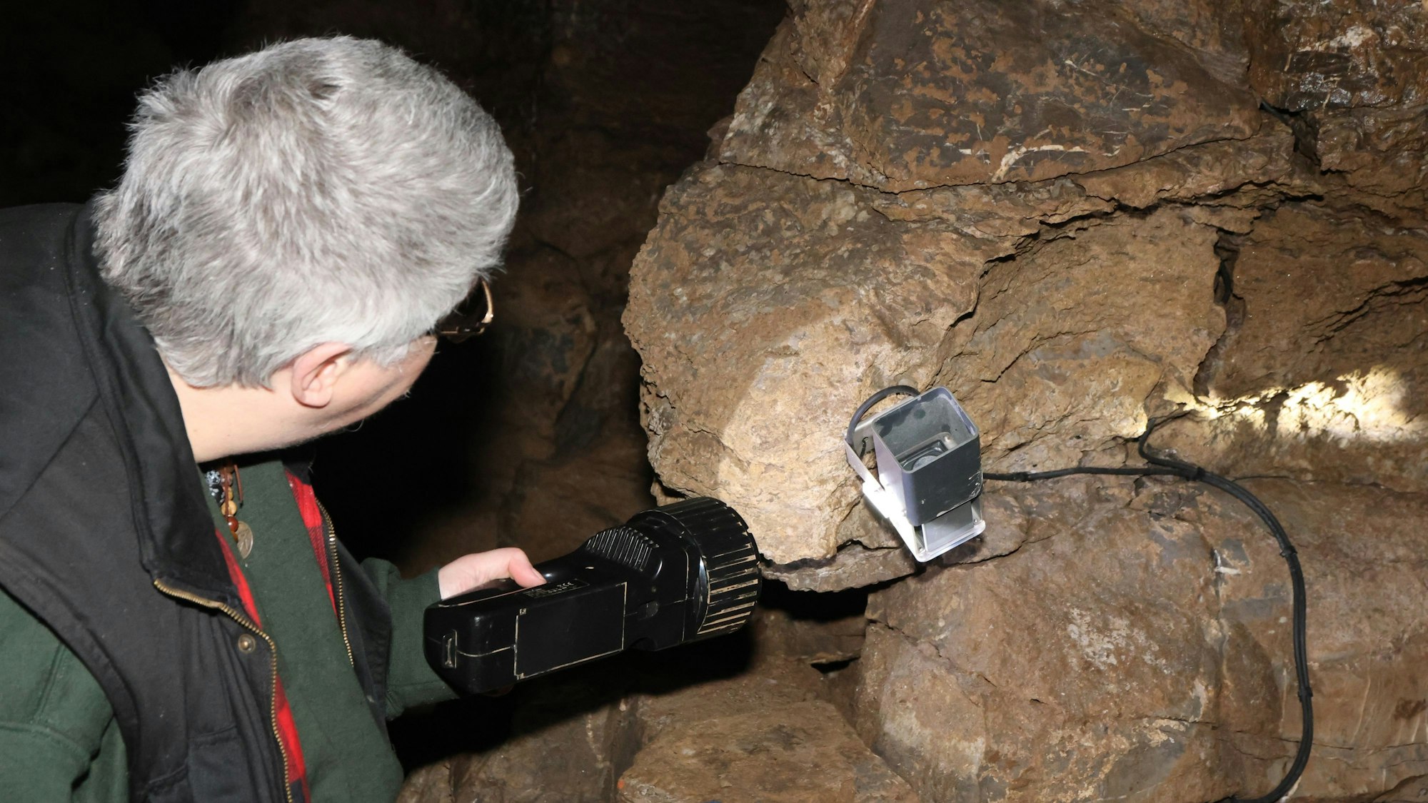 Eine Frau leuchtet in einer Höhle mit einer großen Taschenlampe auf eine defekte Lampe