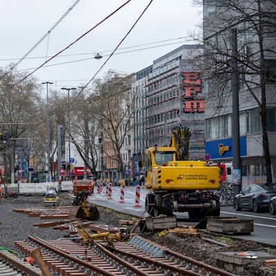 In einem aufgerissenen Gleisbett liegen alte und neue Schienen, Baufahrzeuge stehen daneben.