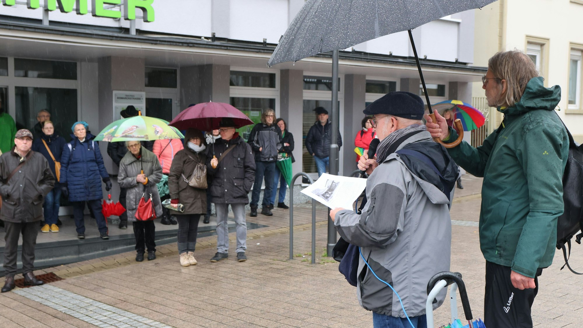 Bei einer Stadtführung stehen Menschen mit Regenschirmen zusammen und lauschen einem Vortragenden.