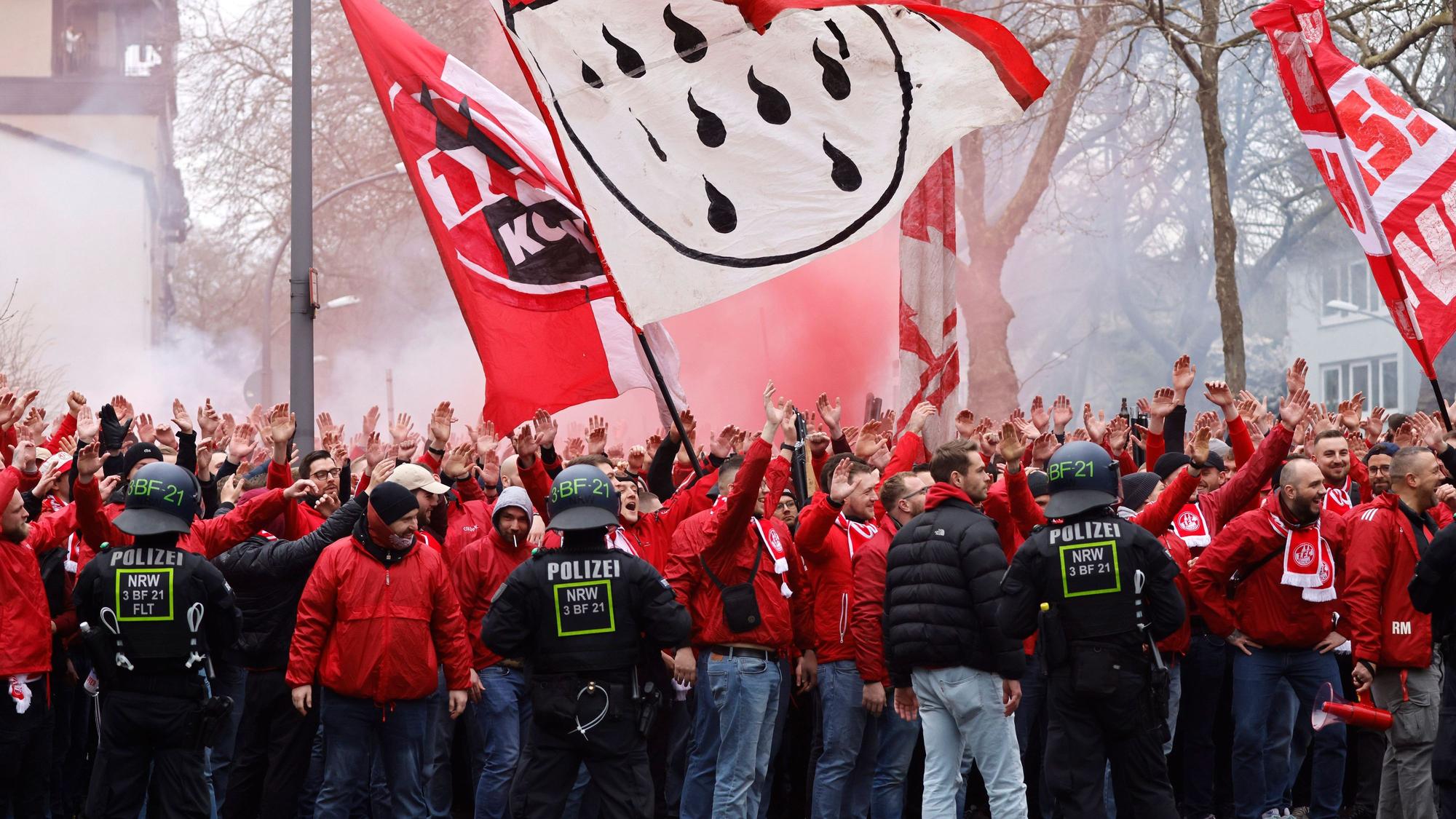FC-Fans marschieren zum Stadion. Sie schwenken Fahnen. Ihr Weg wird gerahmt von Polizisten der Polizei NRW.