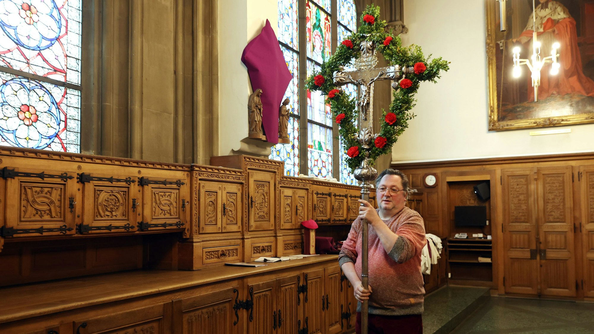 Mann trägt ein mit roten Nelken und Zweigen geschmücktes, großes Silberkreuz vor sich her