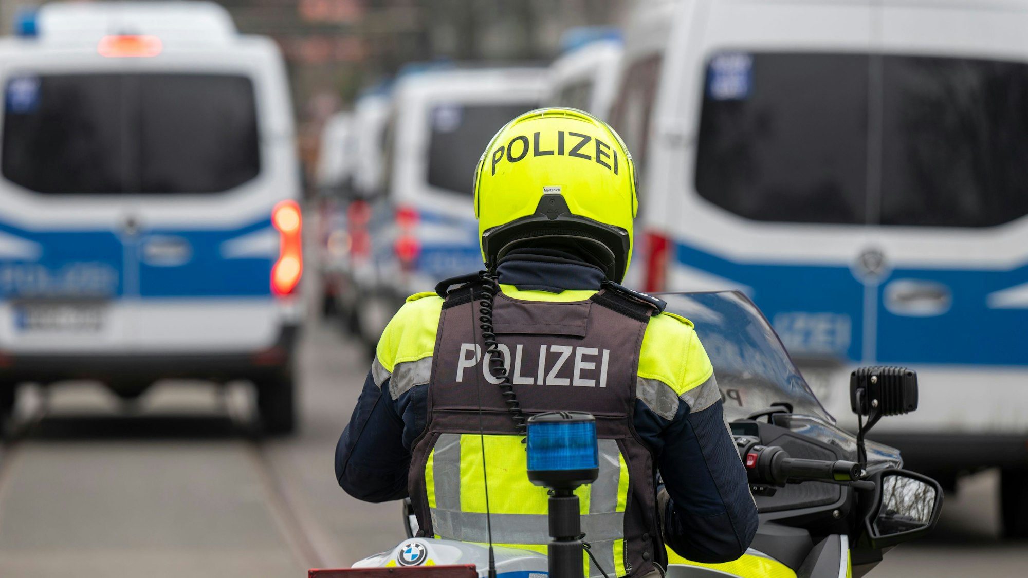 Zu sehen ist ein Polizist auf einem Motorrad. Vor ihm befinden sich mehrere Fahrzeuge der Polizei.
