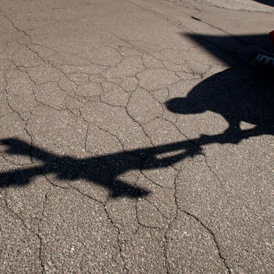 Der Schatten eines Priesters mit einem Kreuz ist auf einem Asphalt zu sehen.