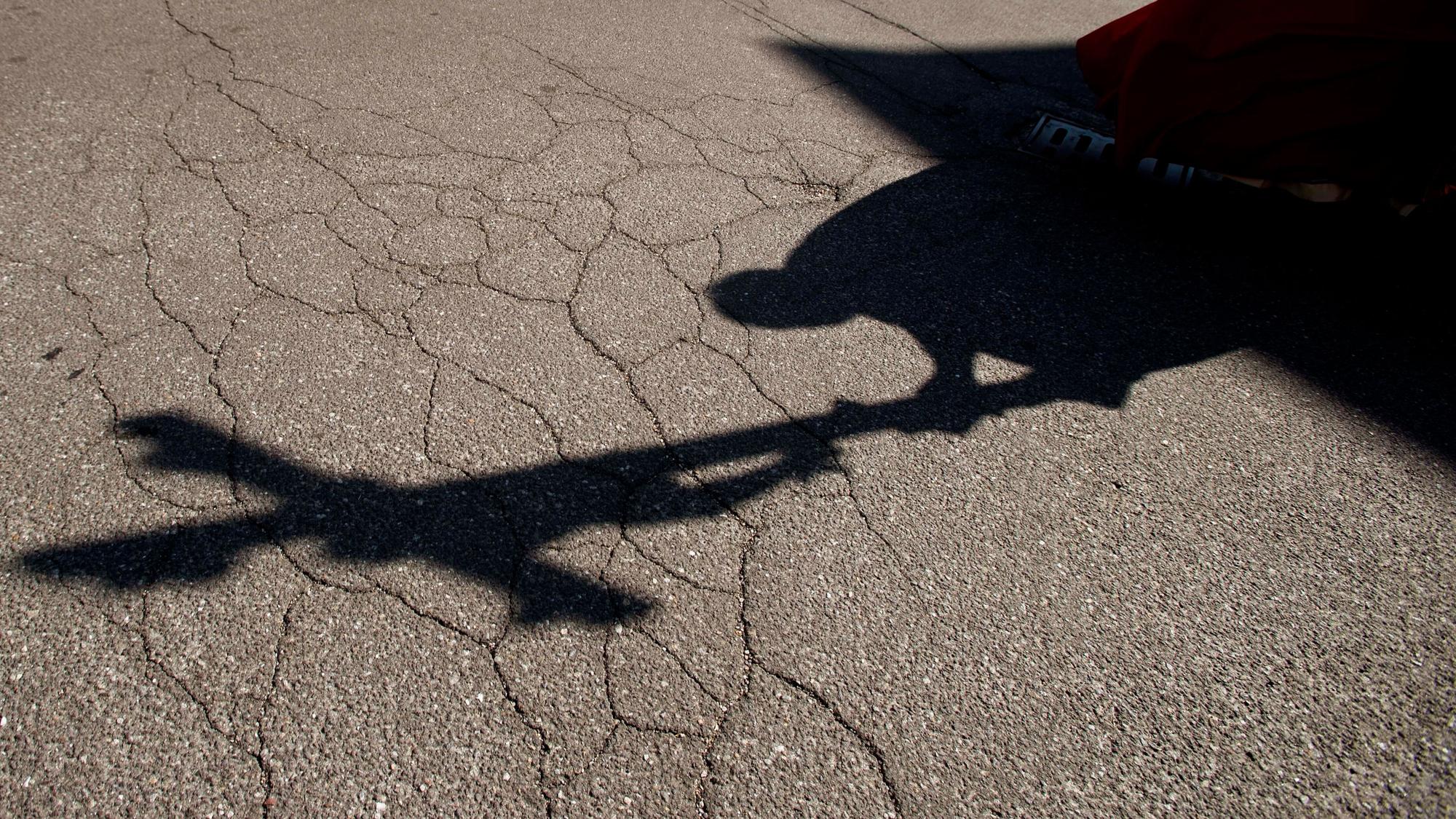 Der Schatten eines Priesters mit einem Kreuz ist auf einem Asphalt zu sehen.