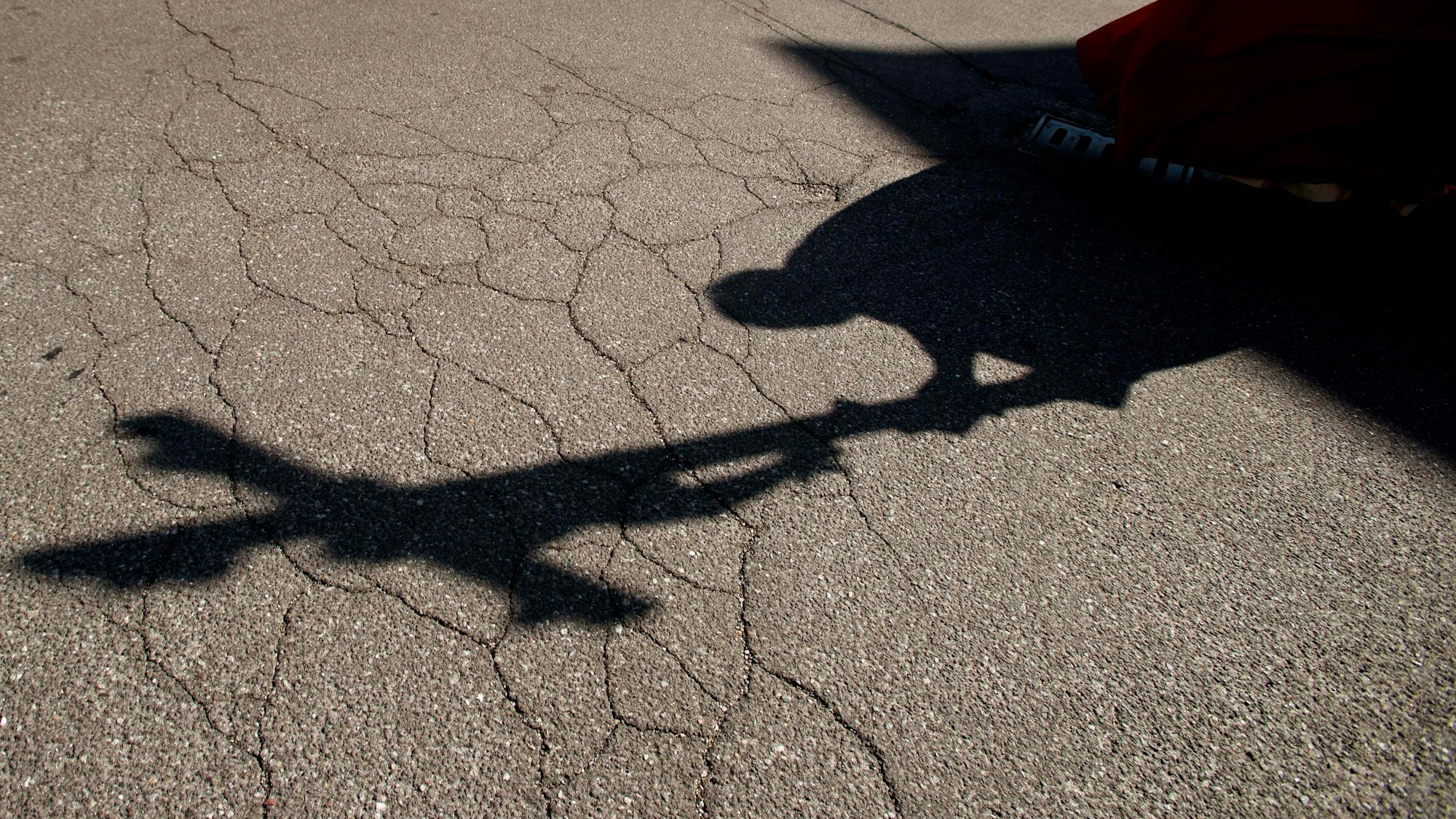 Der Schatten eines Priesters mit einem Kreuz ist auf einem Asphalt zu sehen.