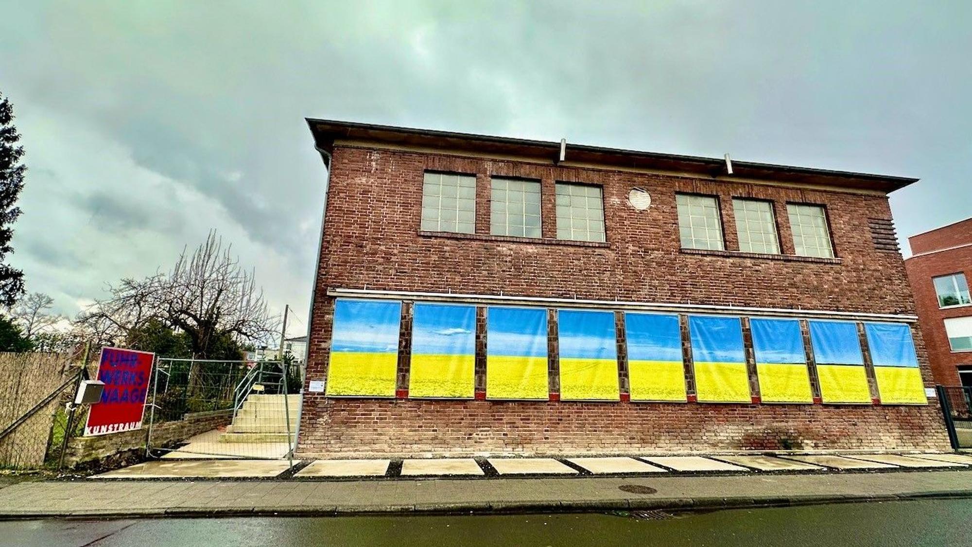 An einem Backsteinhaus hängen ukrainische Flaggen.