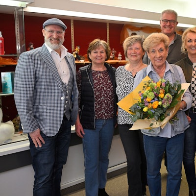 Ingrid Wilms steht mit ihren Mitarbeiterinnen und ihrer Familie im Laden. Sie hält einen Blumenstrauß in den Händen.