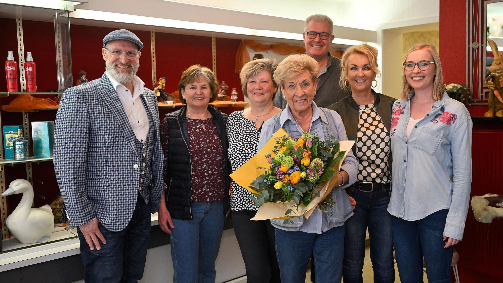 Ingrid Wilms steht mit ihren Mitarbeiterinnen und ihrer Familie im Laden. Sie hält einen Blumenstrauß in den Händen.