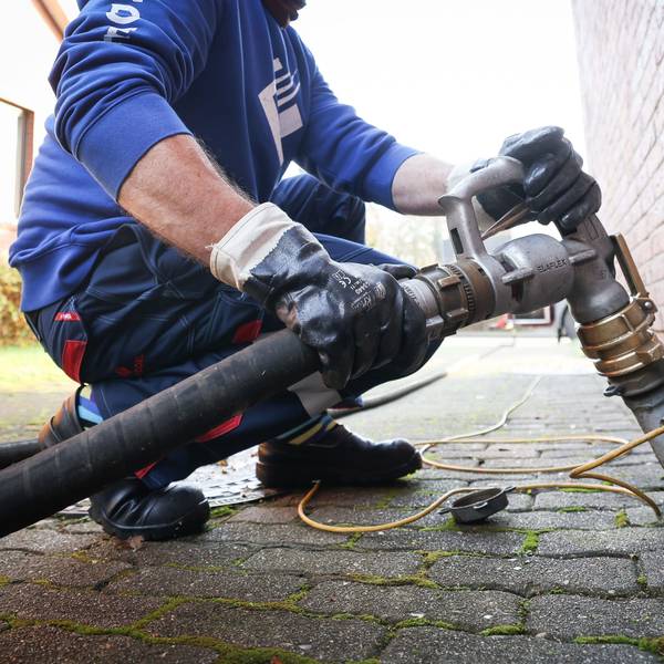 Ein Mitarbeiter eines Diesel- und Heizöl-Unternehmens befestigt die Zapfpistole an einem Füllstutzen für die Heizöllieferung an einen Kunden in einem Einfamilienhaus.