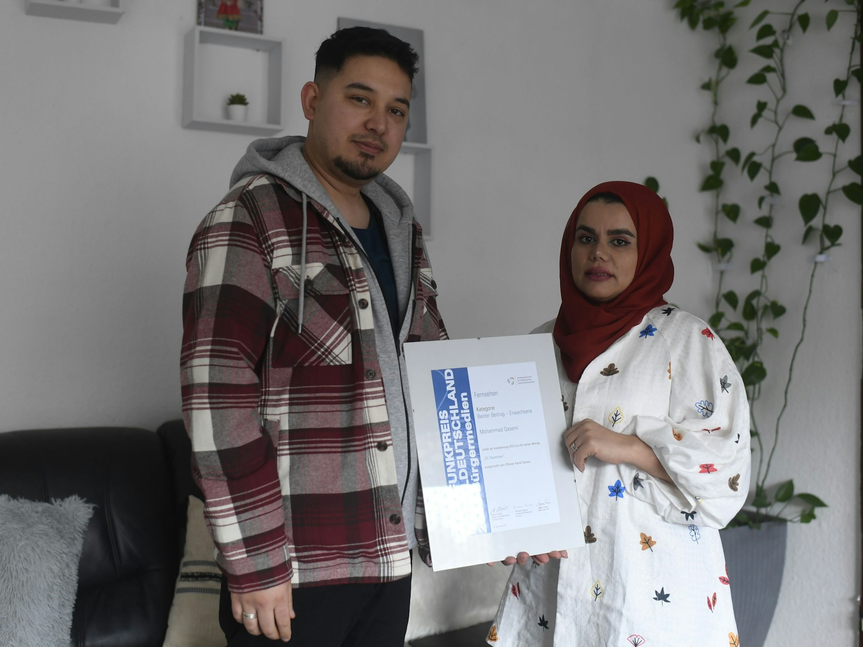 Qasemi und Nahida Mohammadi stehen in ihrer Wohnung und halten eine gerahmte Auszeichnung.
