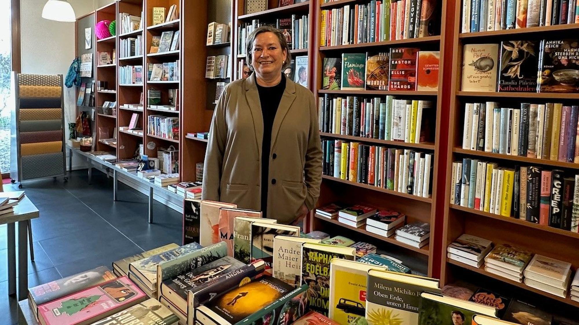 Die Buchhändlerin steht vor ihren Regalen.