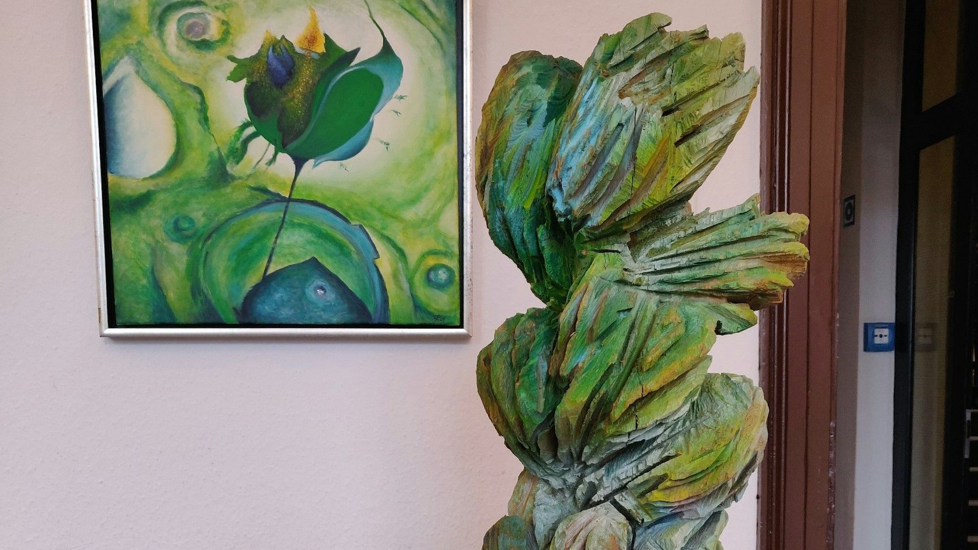 Holzskulptur „Eruption“ von Riccarda Menger vor einem floralen Motiv von Ulla Pützstück.