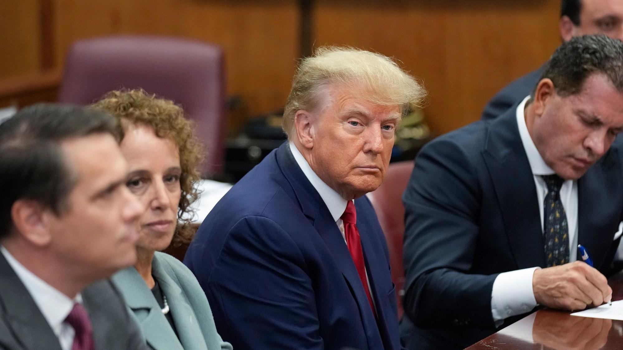 Donald Trump (M), ehemaliger Präsident der USA, sitzt in einem Gerichtssaal in Manhattan mit seinem Verteidigungsteam am Tisch.