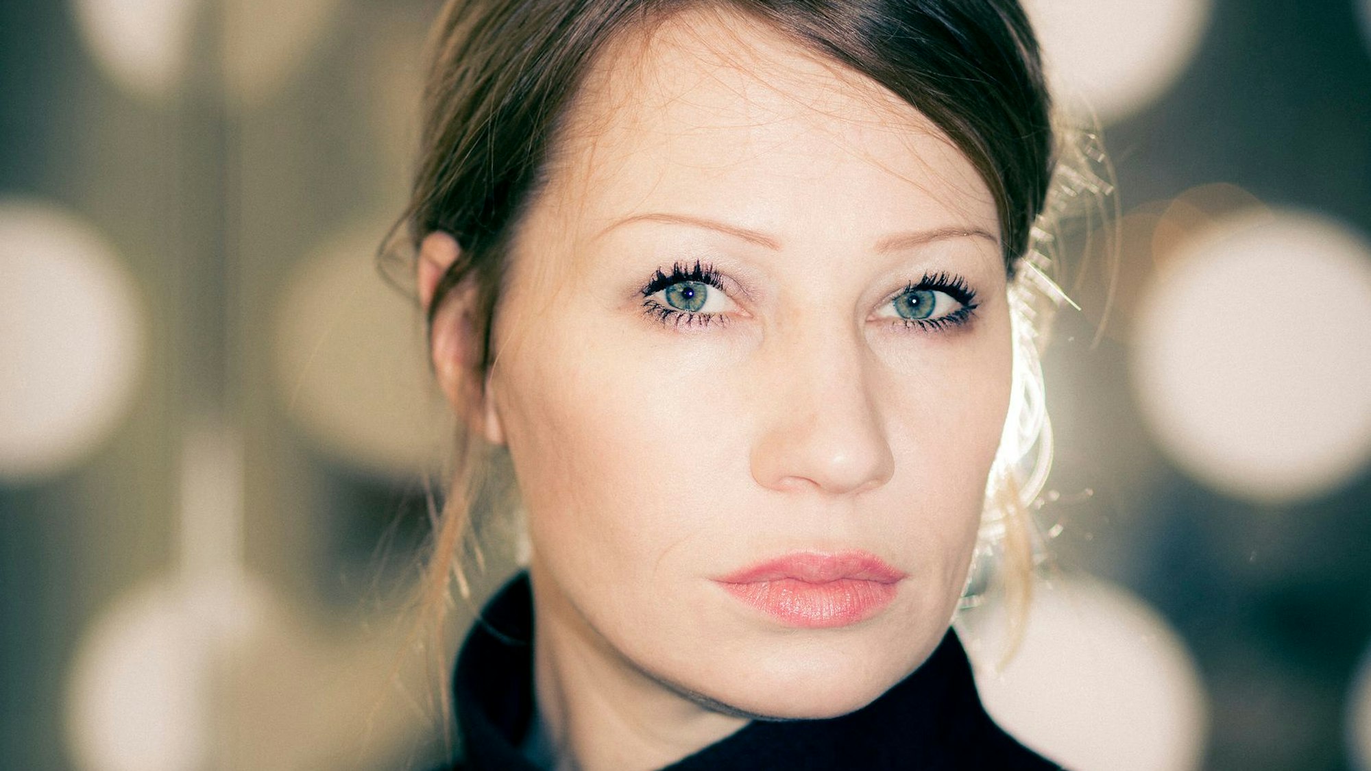 Birgit Minichmayr schaut ernst in die Kamera. Sie hat blaue Augen. Der Hintergrund ist unscharf.