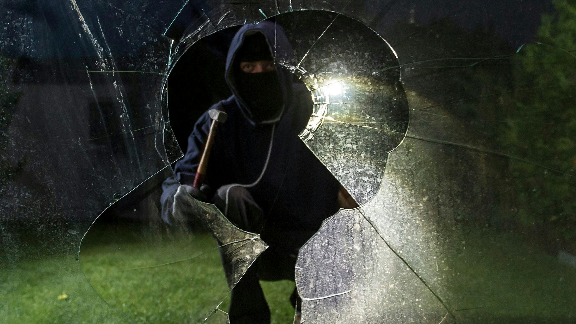 Gesprungene Fensterscheibe, dahinter symbolischer Einbrecher