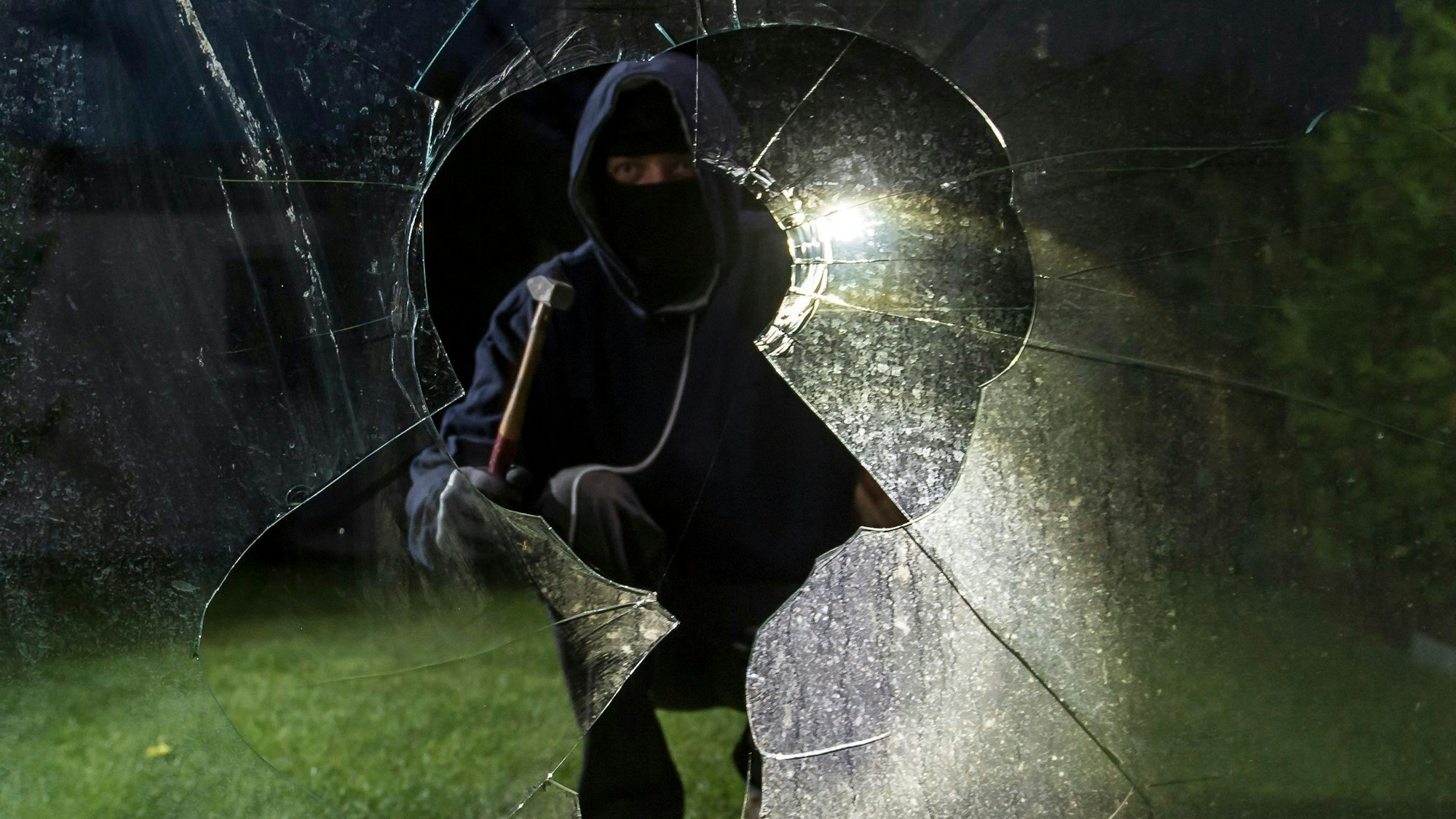 Gesprungene Fensterscheibe, dahinter symbolischer Einbrecher