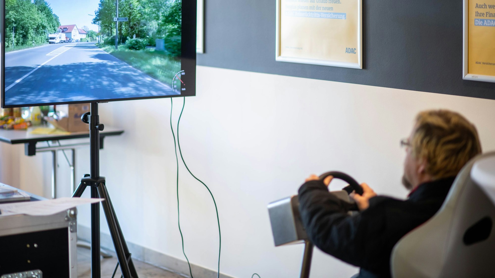 Ein Mann bedient einen Fahrsimulatur und schaut auf einen Bildschirm, der eine Straße anzeigt.