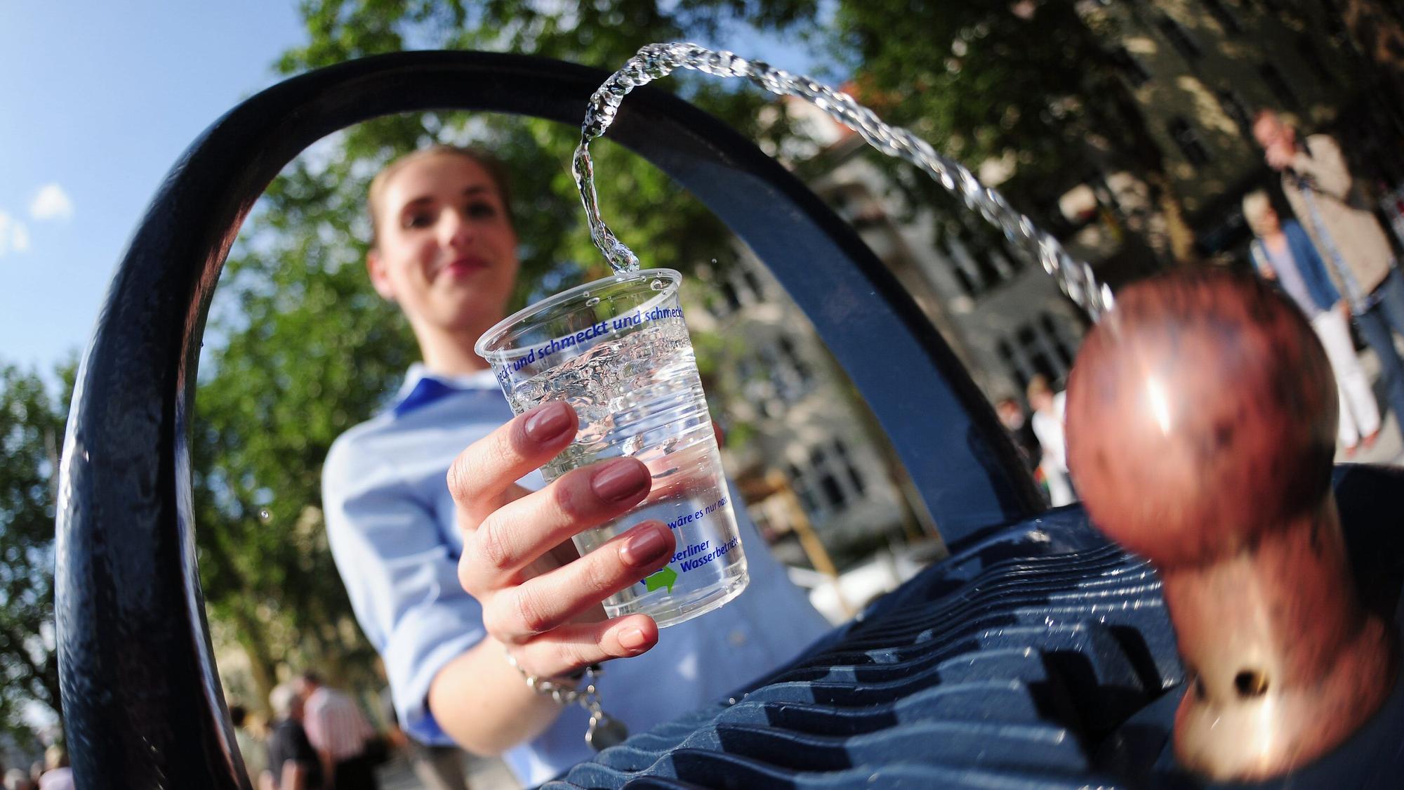 Eine junge Frau nimmt Wasser von einem Trinkbrunnen.