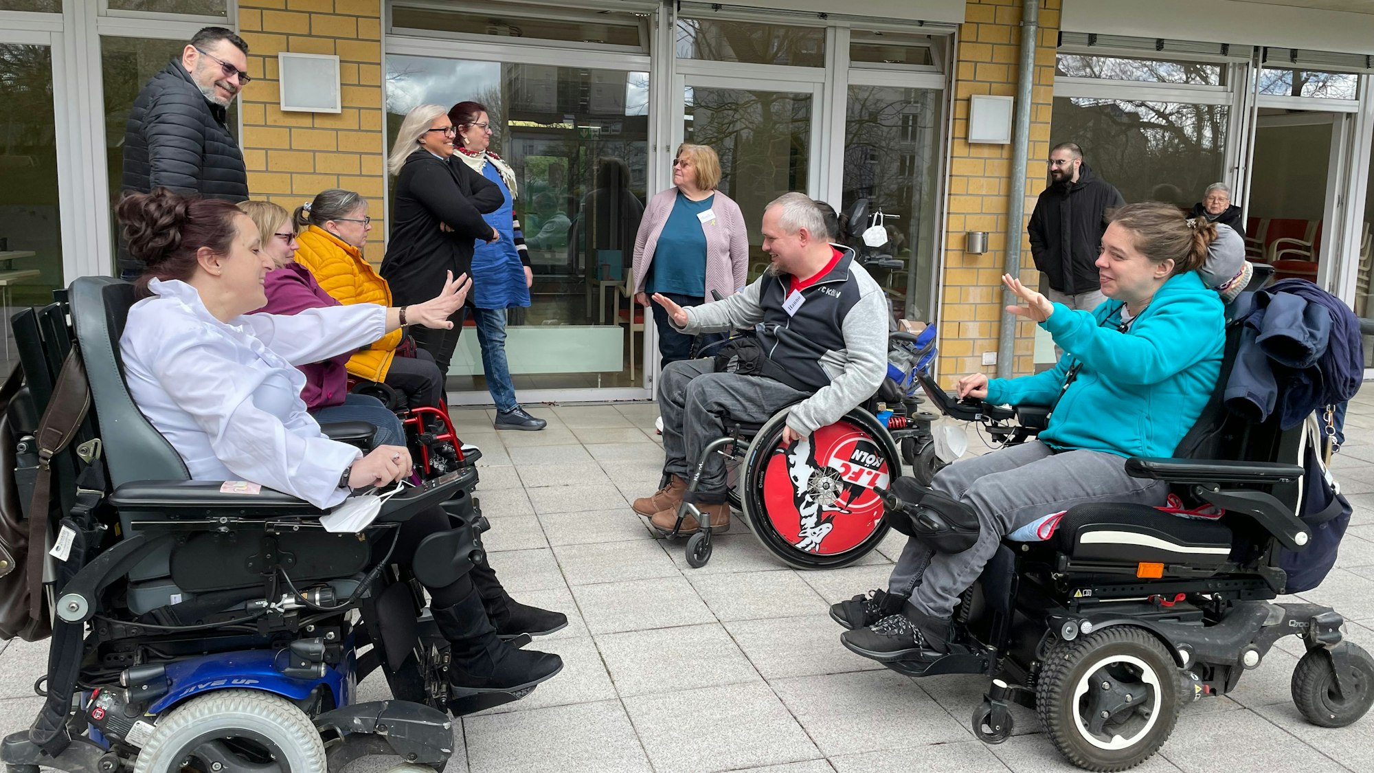 Männer und Frauen in Rollstühlen sitzen sich gegenüber und lächeln.