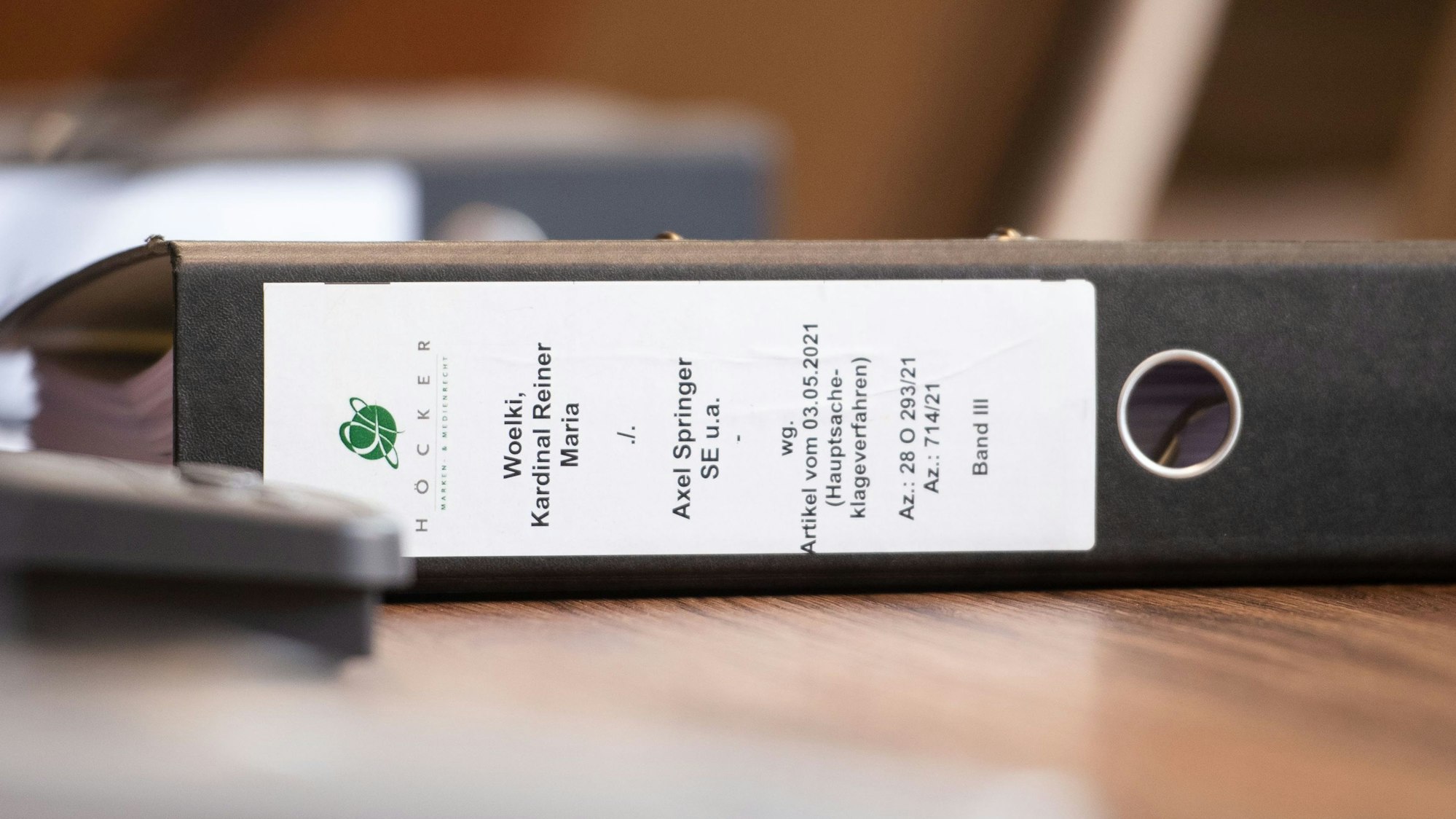 Auf einem Tisch liegt ein Aktenordner, dessen Rücken beschriftet ist: „Woelki, Kardinal Rainer Maria ./. Axel Springer SE u.a. wg. Artikel vom 3.5.2021“.