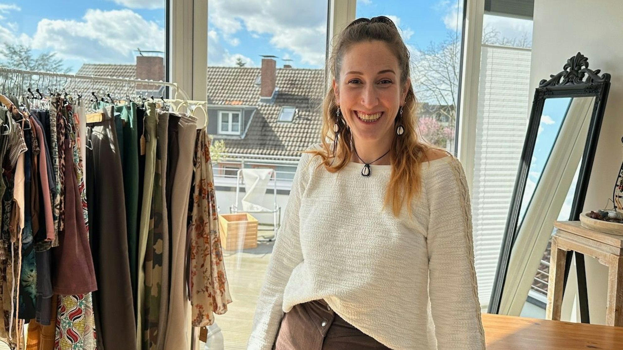 Die Designerin steht vor einer Kleiderstange.