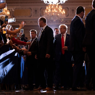 Es ist eine Menschenmenge zu sehen. Trump läuft durch die Mitte dieser.