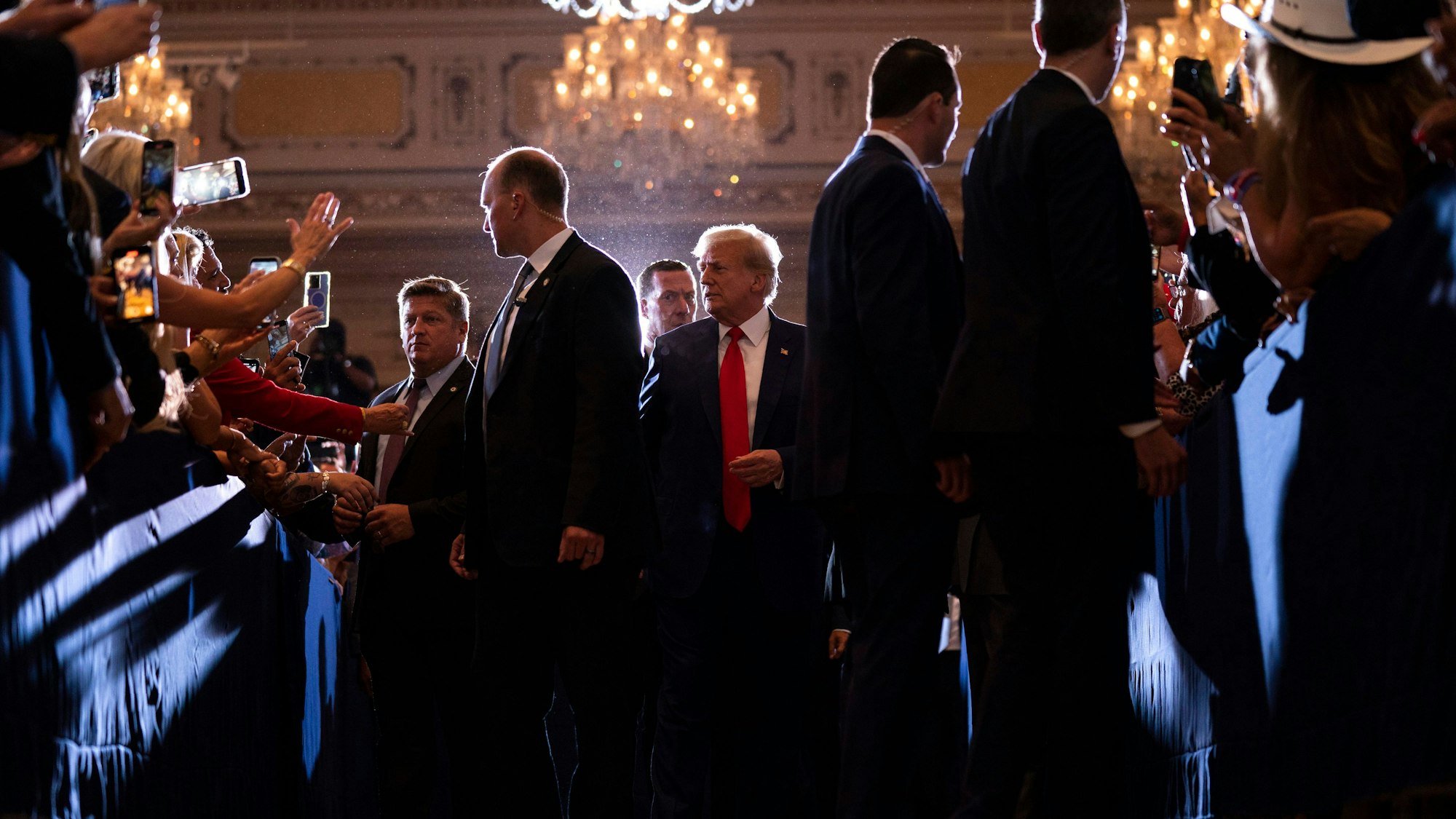 Es ist eine Menschenmenge zu sehen. Trump läuft durch die Mitte dieser.