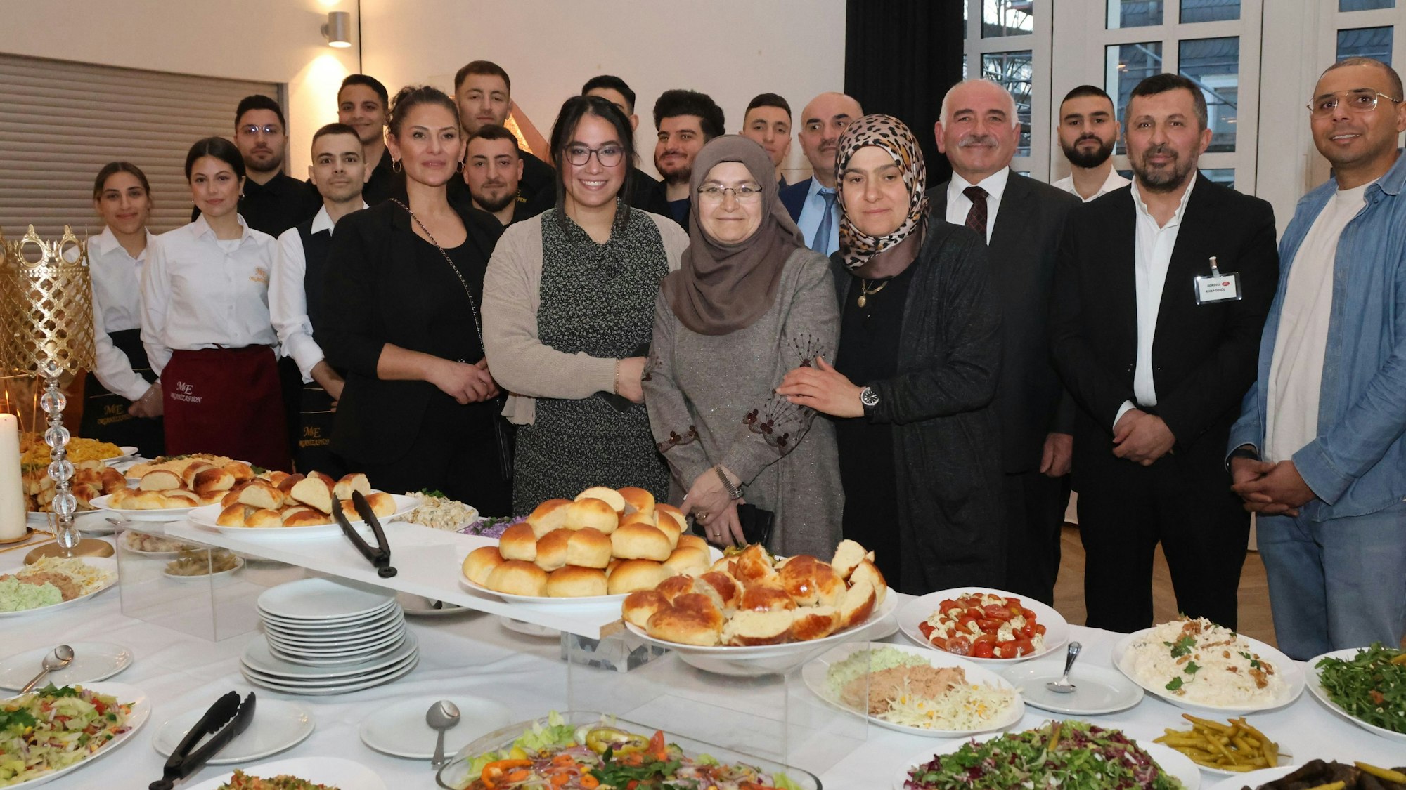 Blick auf eine Menschengruppe, davor eine mit Speisen reich gedeckten Tafel.