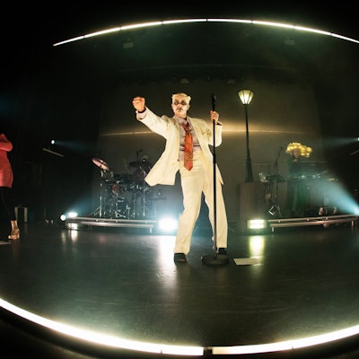 Fever Ray, alias Karin Dreijer, im weißen Anzug auf der Bühne unter einer Laterne.