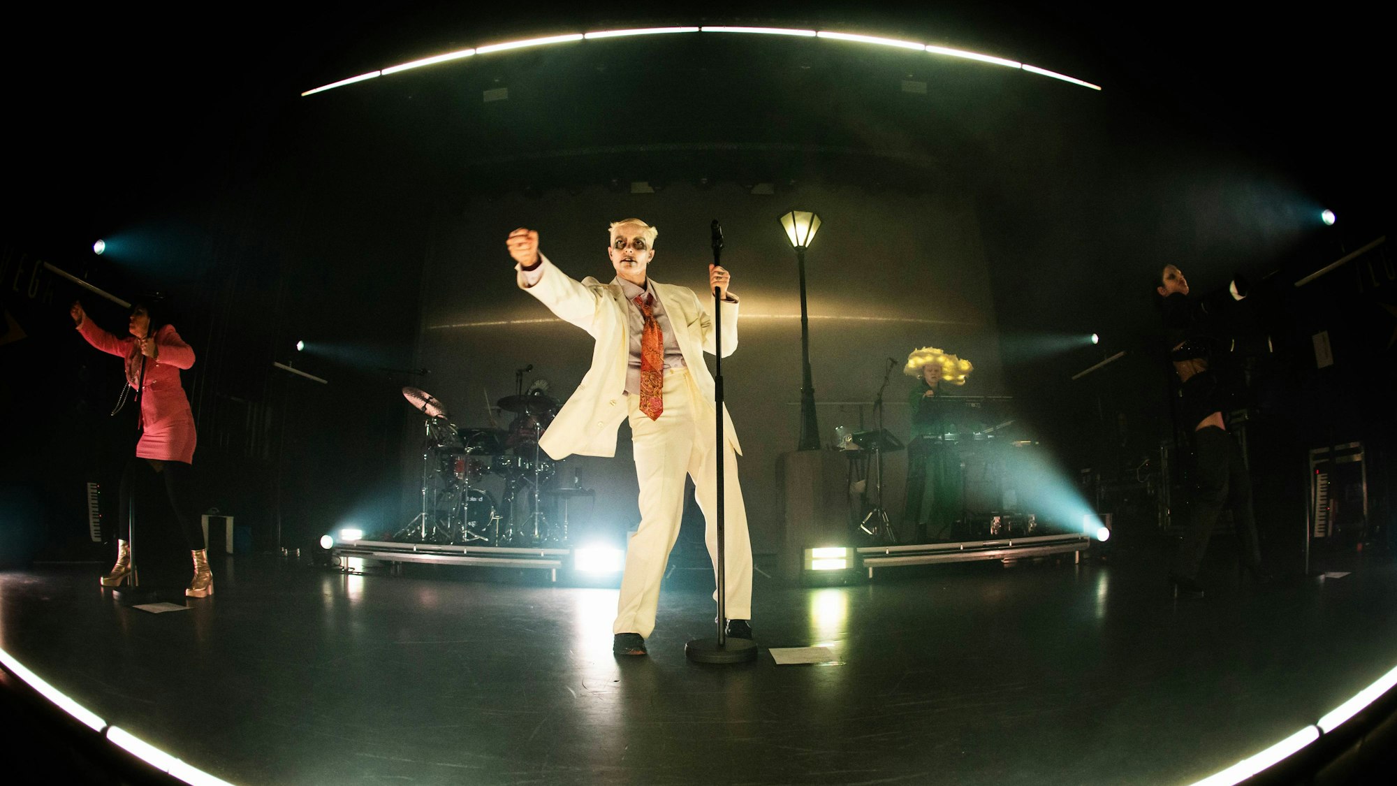 Fever Ray, alias Karin Dreijer, im weißen Anzug auf der Bühne unter einer Laterne.