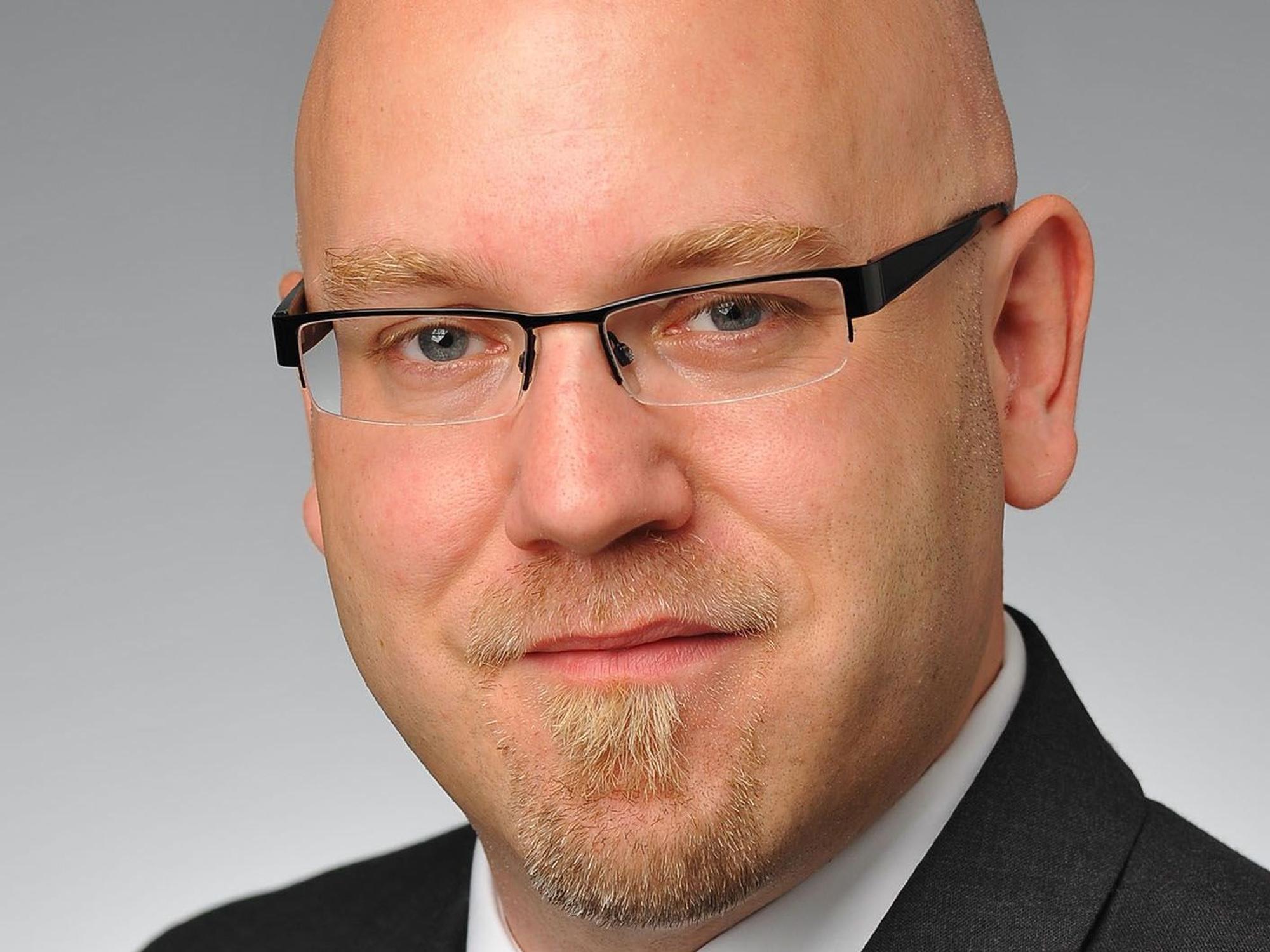 Stefan Reimers guckt für ein Porträtfoto in dei Kamera. Er trägt einen Anzug und eine Brille.