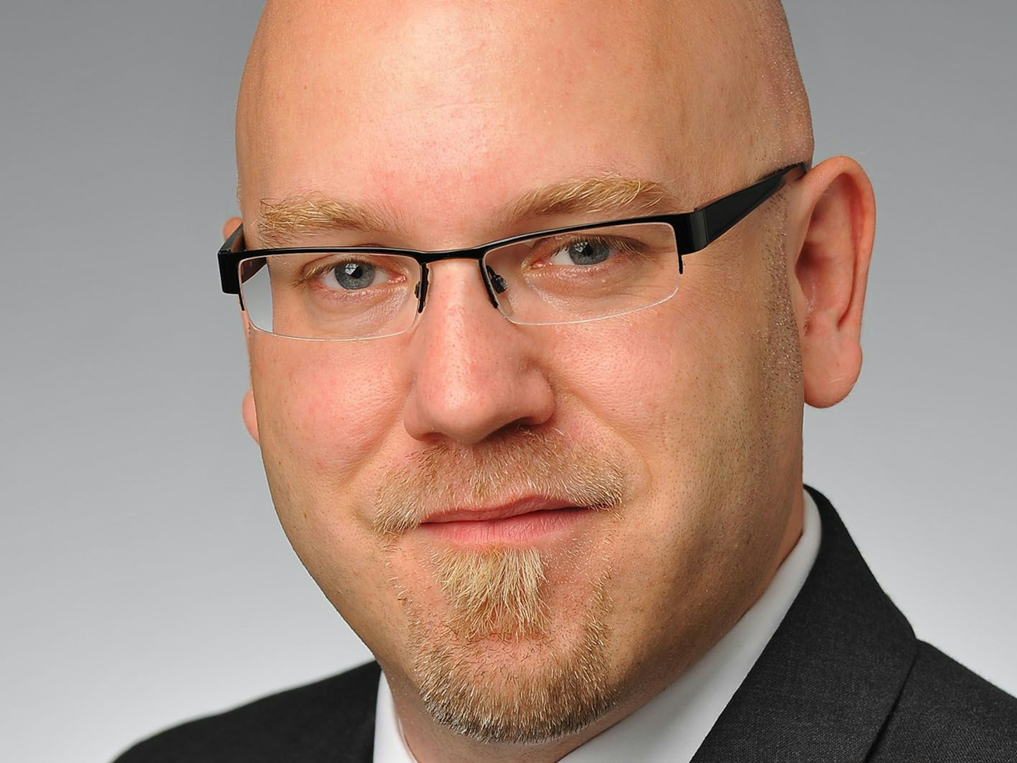 Stefan Reimers guckt für ein Porträtfoto in dei Kamera. Er trägt einen Anzug und eine Brille.