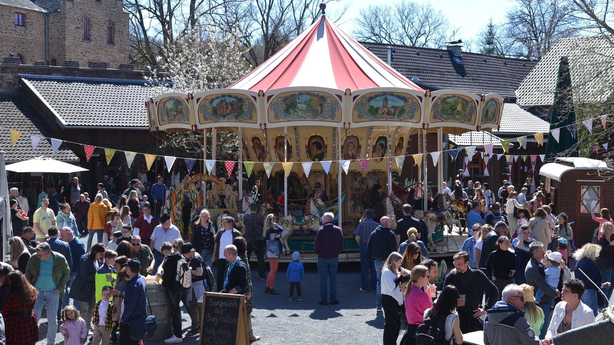 Tausende Besucher schlenderten über den Ostermarkt auf Burg Satzvey. In der Mitte des Bildes ist ein Karussell zu sehen.