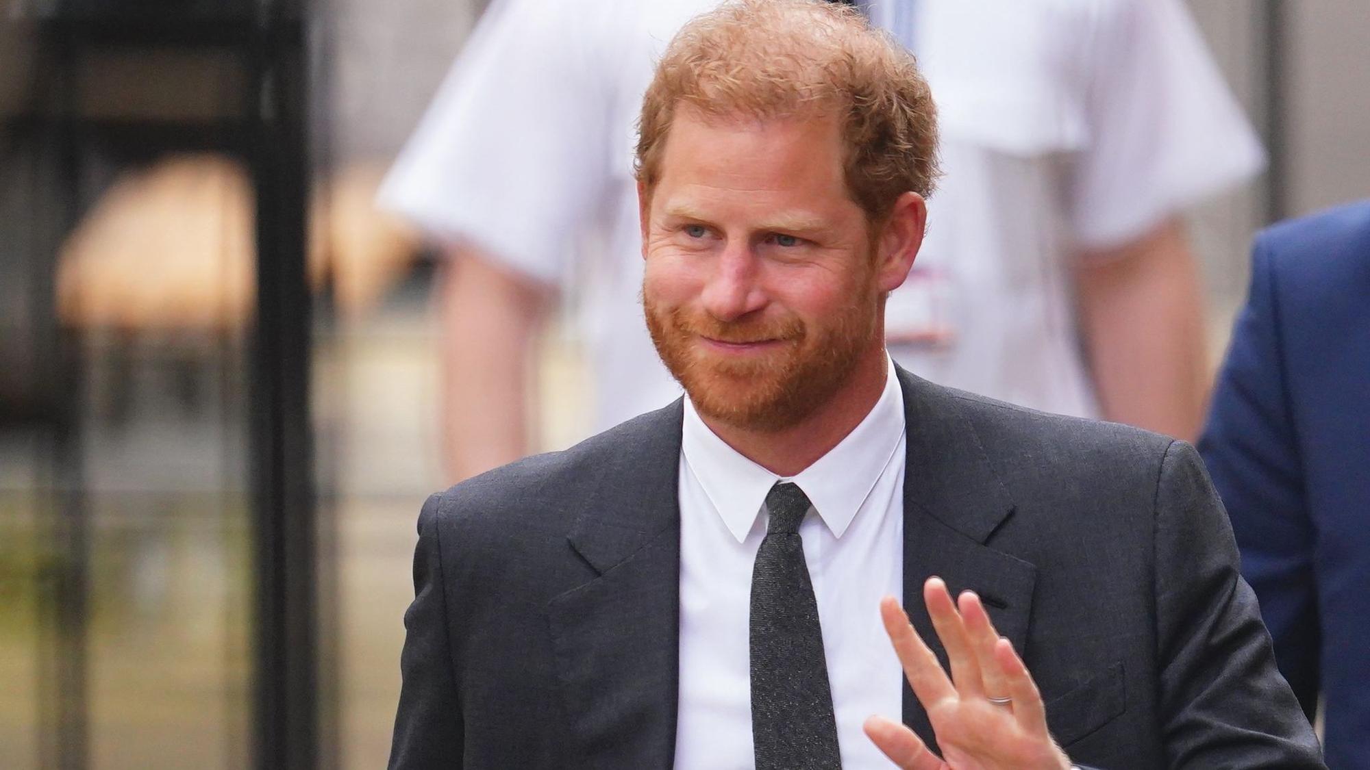 Prinz Harry auf dem Weg ins Gericht. Er hebt seine Hand zu einem Gruß.