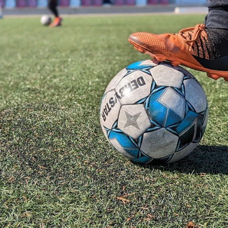 Das Bild zeigt einen Fußball auf dem durch Bengalos beschädigten Kunstrasenplatz.