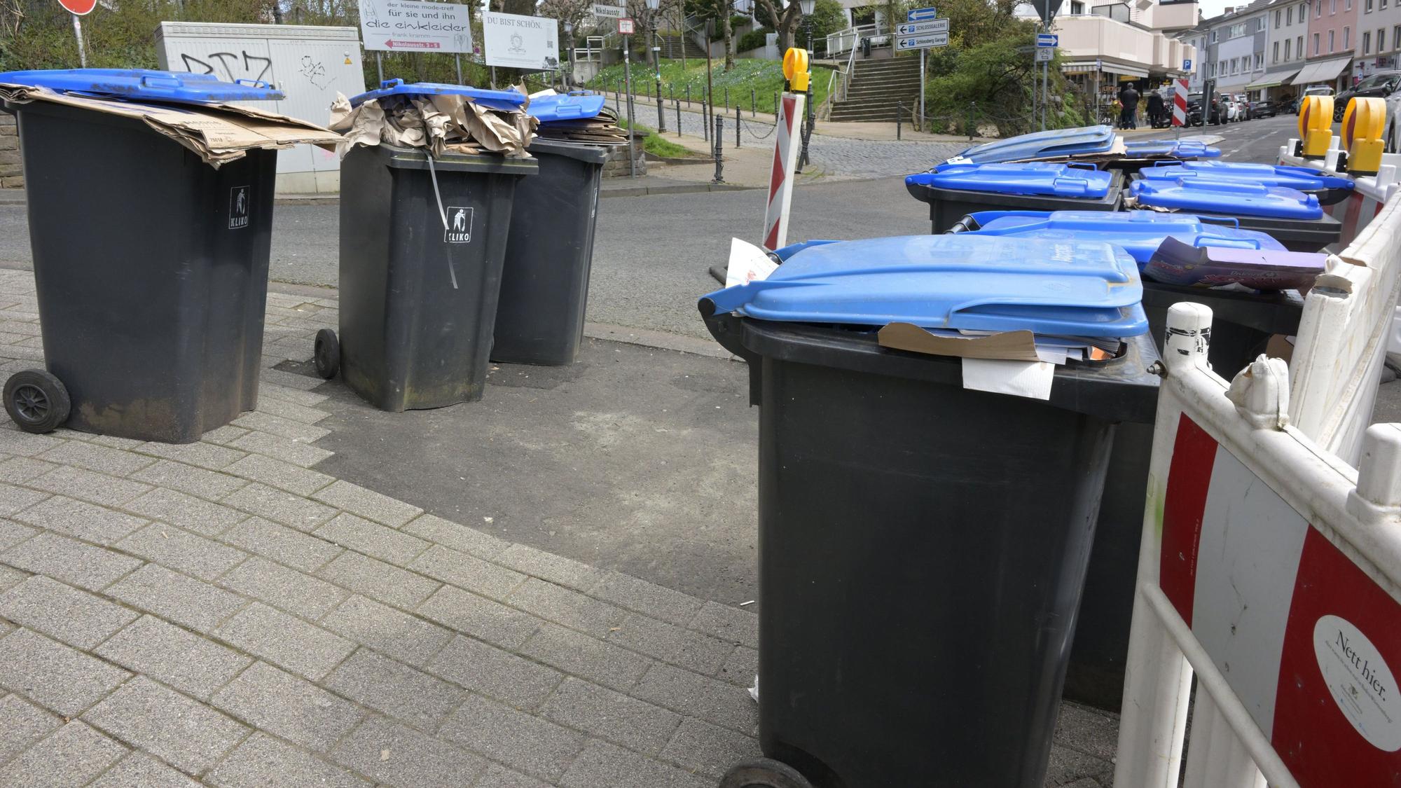 Mehrere Papiermülltonnen stehen ungeleert nebeneinander.