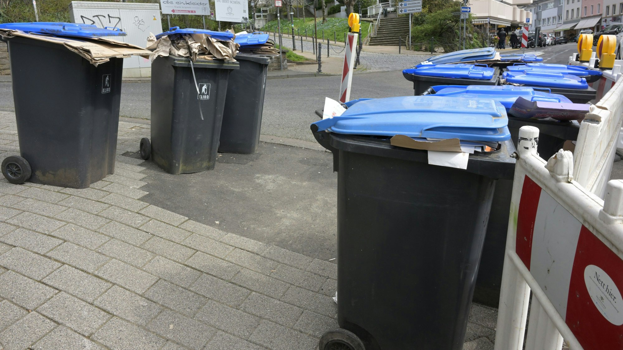 Mitten auf dem Fußweg stehen mehrere Papier-Mülltonnen.