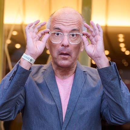 Schauspieler Christoph Maria Herbst zieht eine große Brille mit weißem Rand auf seiner Nase theatralisch nach vorne.