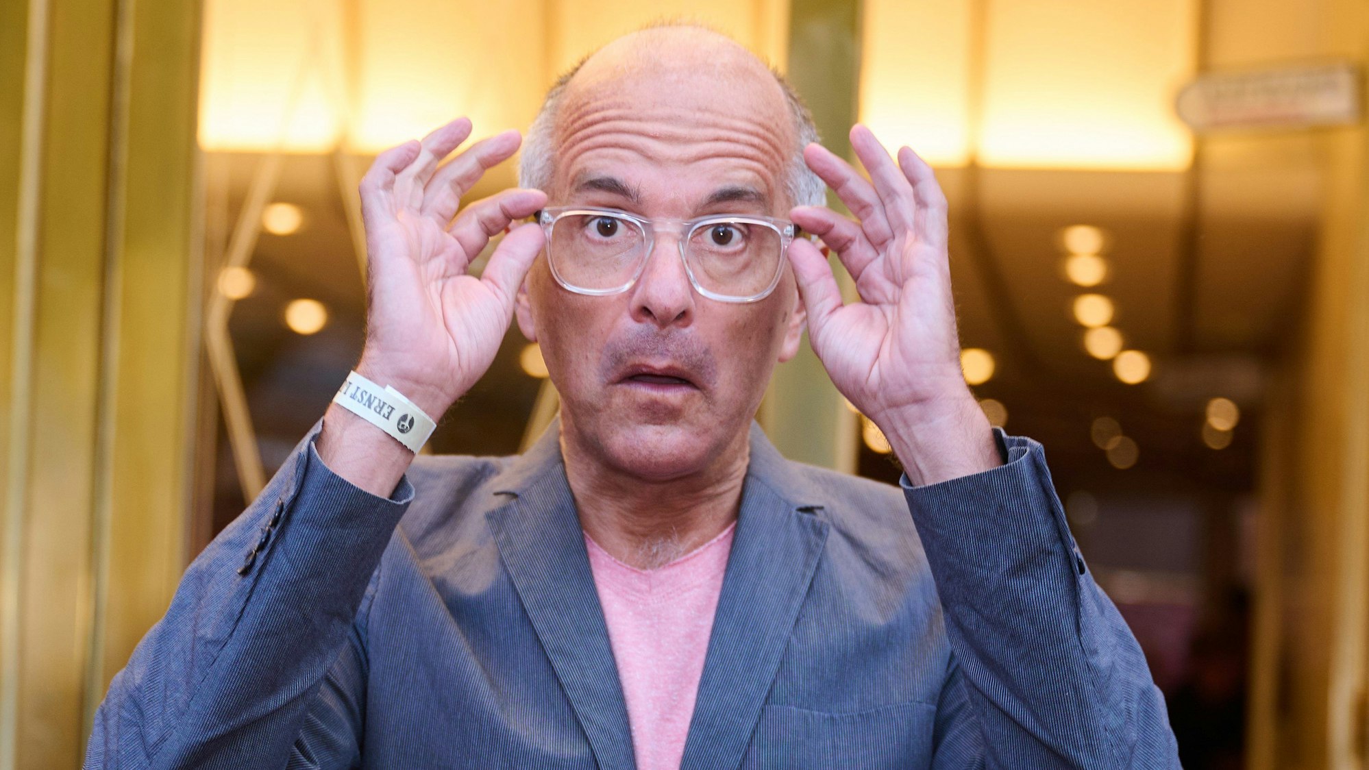 Schauspieler Christoph Maria Herbst zieht eine große Brille mit weißem Rand auf seiner Nase theatralisch nach vorne.