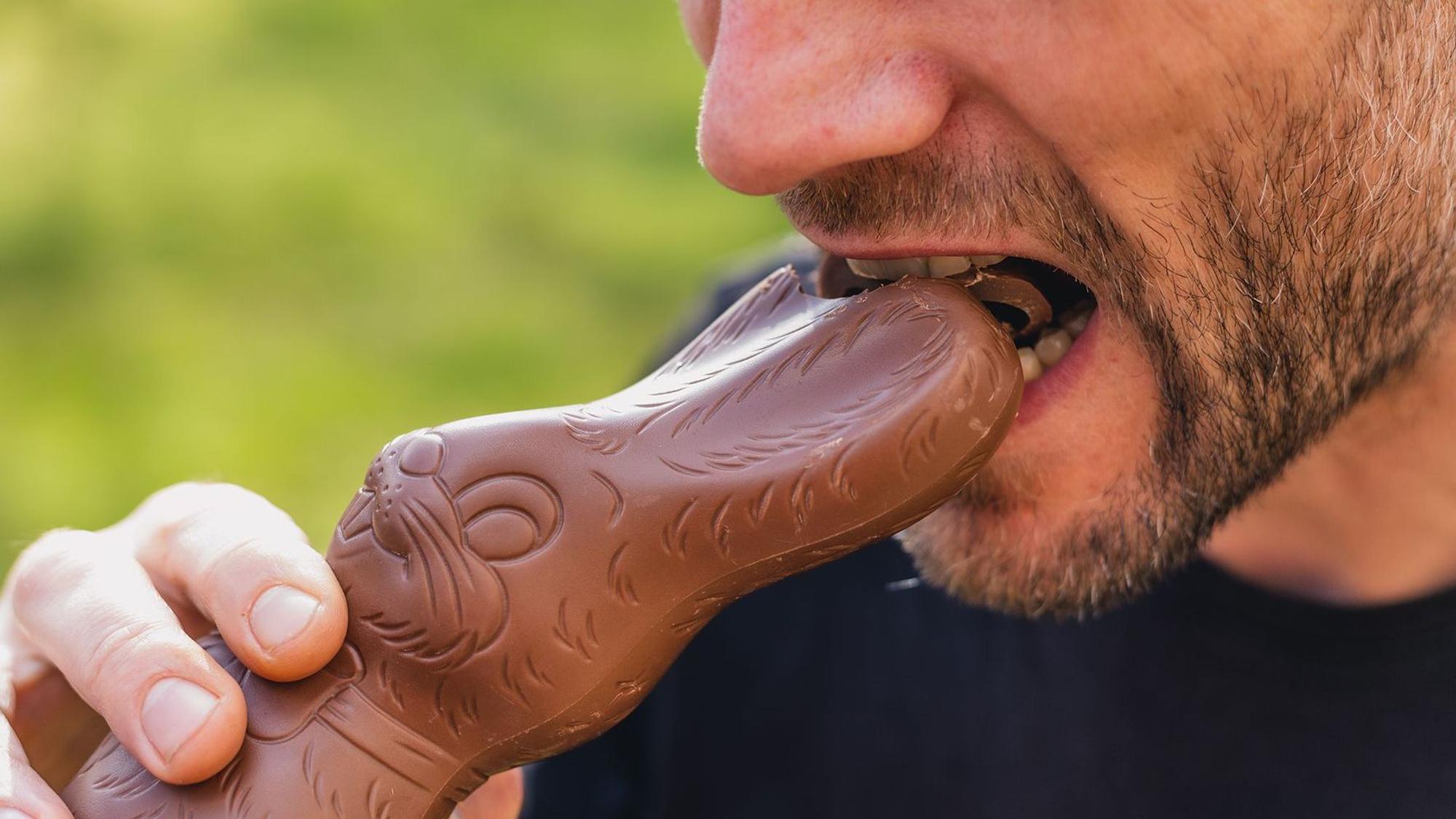 Ein Mann beißt in einen Schokohasen.
