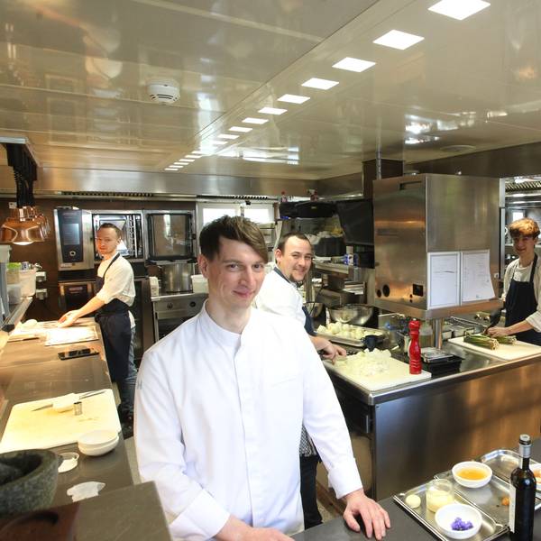 Thomas und sein Team lächeln in die Kamera und stehen an verschiedenen Stationen in der Küche.