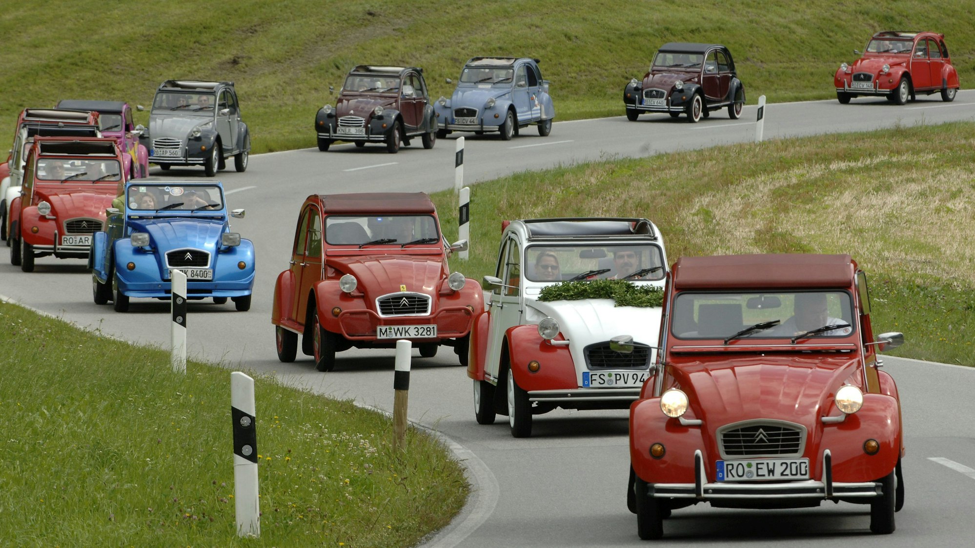Dicht an dicht fahren diverse Citroën 2CV, die sogenannten Enten, auf einer Straße in der Nähe der oberbayerischen Ortschaft Windshausen