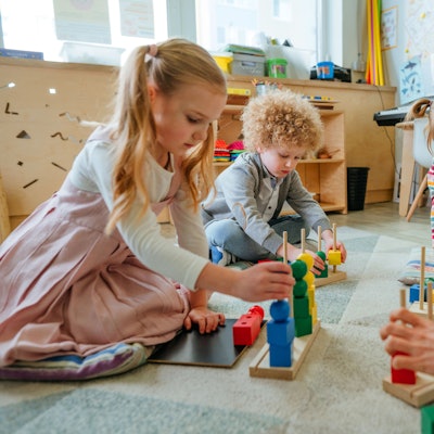 Drei Kinder sitzen im Innenraum eines Kindergarten auf dem Boden und spielen mit Bauklötzen.