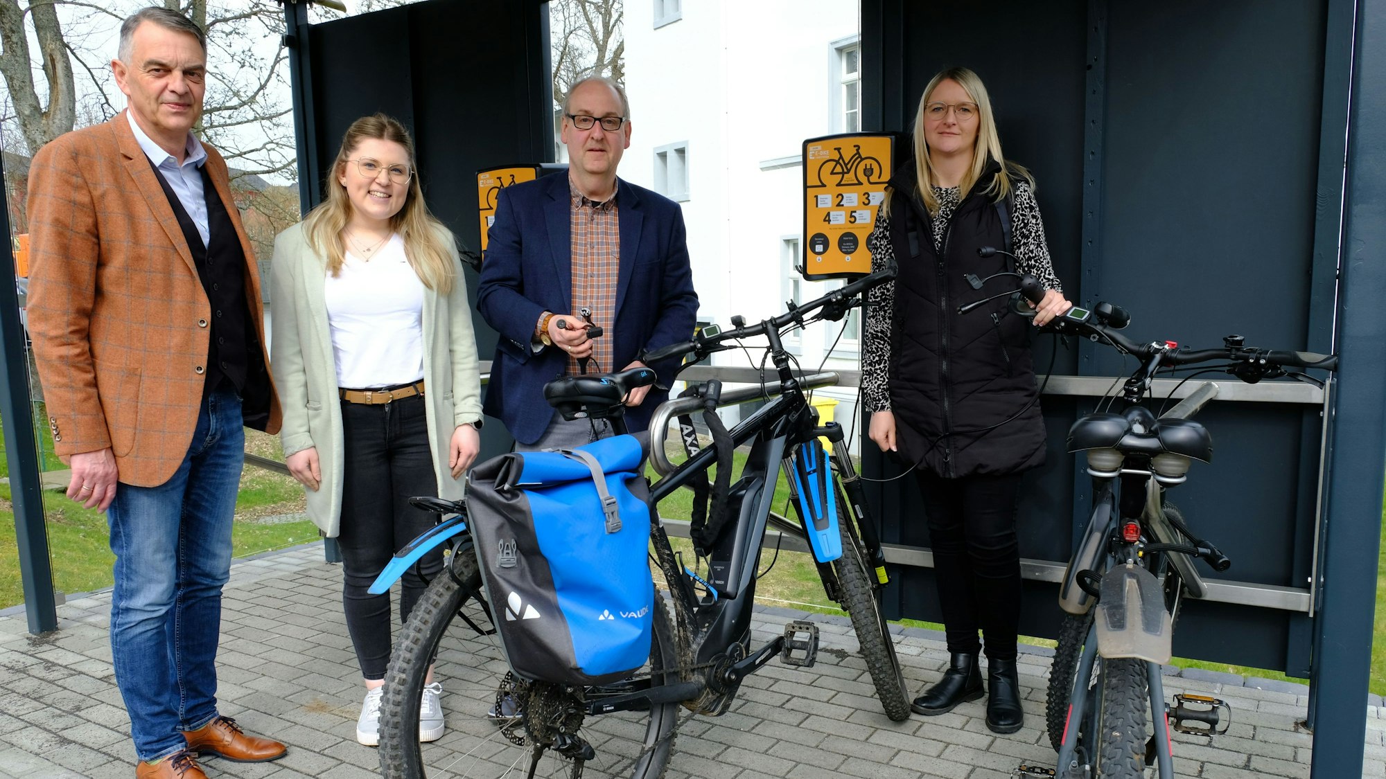 Zwei Männer und zwei Frauen stehen mit Fahrrädern an der E-Bike-Ladestation in Hellenthal.
