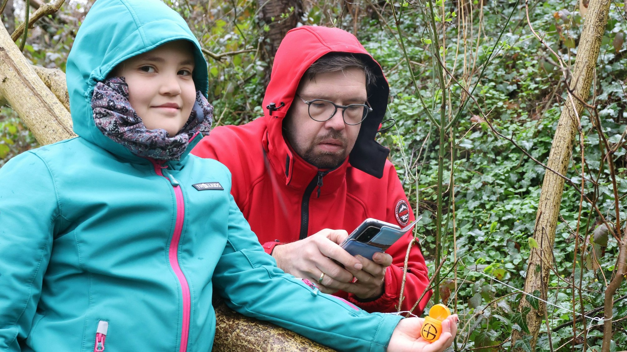 Zu sehen sind ein zehnjähriges Mädchen mit ihrem Vater in der Natur bei der Ostereiersuche. Es regnet.